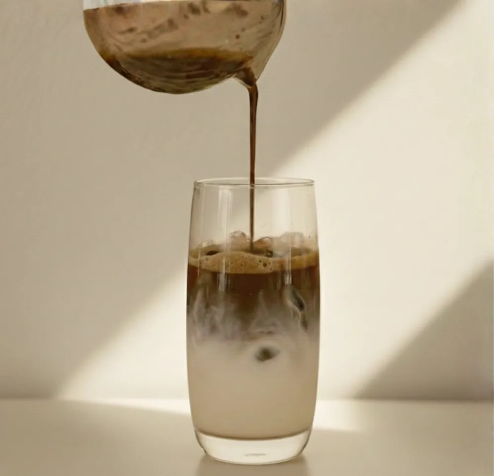 Hojicha poured from a glass jug over milk and ice in a tall glass, in afternoon light