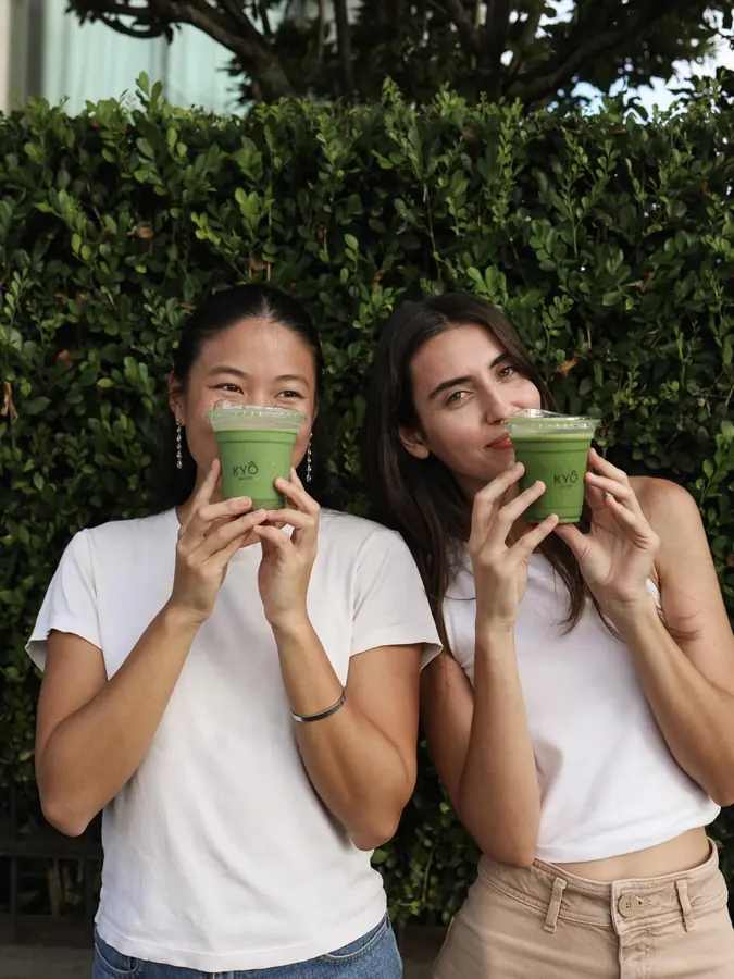 Two friends sipping matcha together in front of greenery