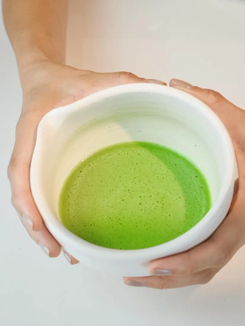 Two hands holding a white bowl of freshly whisked matcha