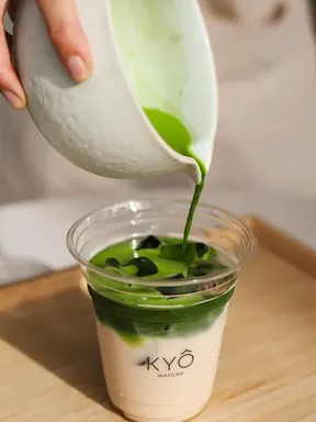Matcha poured from a white bowl into a KYÔ cup of milk and ice