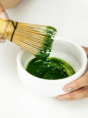 A bamboo chasen whisking deep green matcha in a white bowl