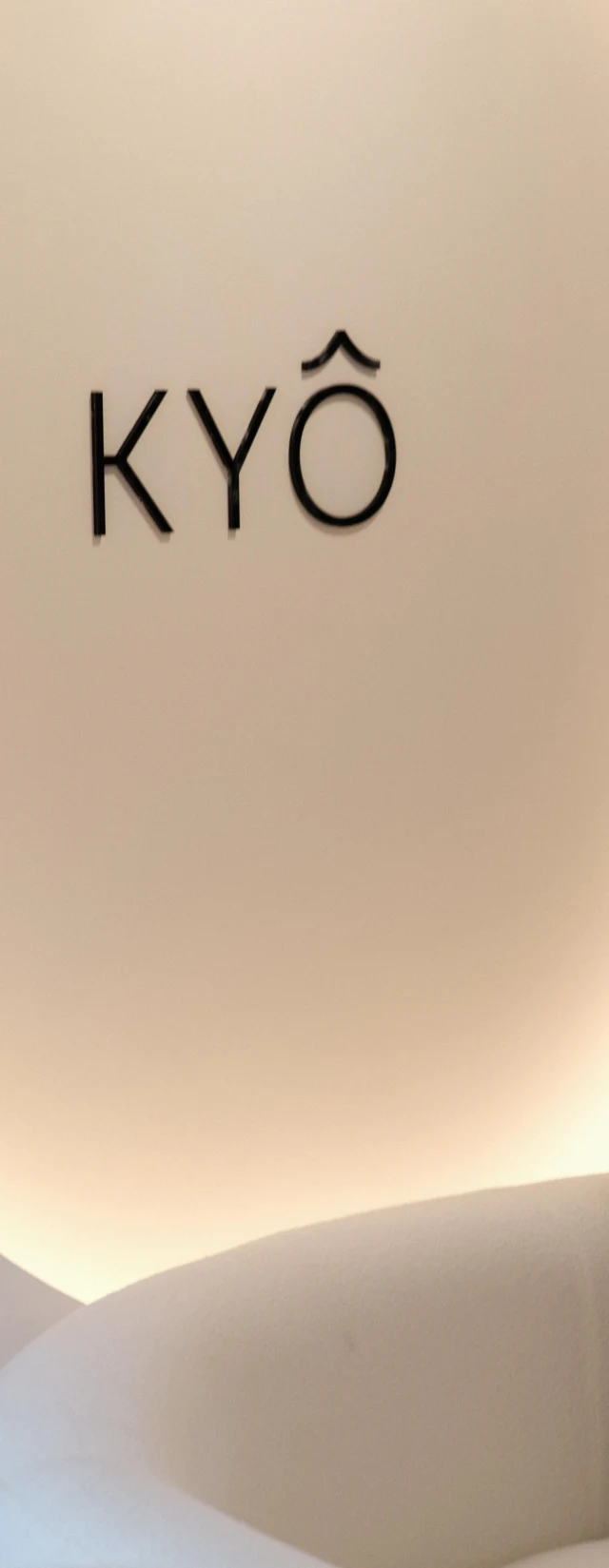 The KYÔ logo on a backlit halo of light, over a cream sofa