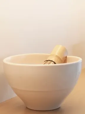 White matcha bowls with bamboo whisks on light oak shelves, lit from beneath