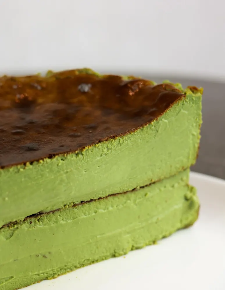 A wedge of matcha basque burnt cheesecake, bright green inside under a caramelised top